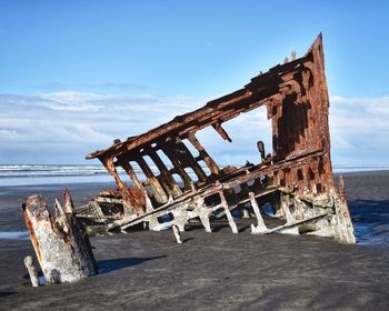 Old wooden posts on beach against sky