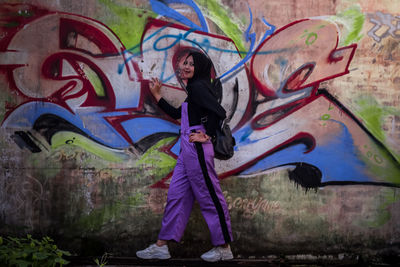 Full length of teenage boy standing against graffiti wall