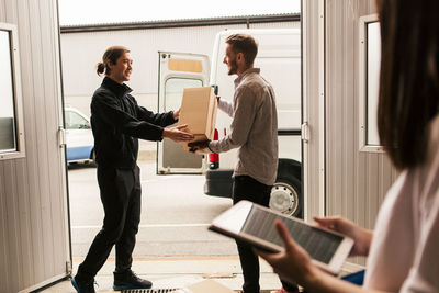 Female using digital tablet while male coworkers delivering boxes in van