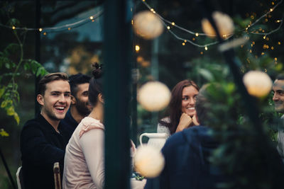 Happy multi-ethnic young friends sitting at dining table during party in back yard