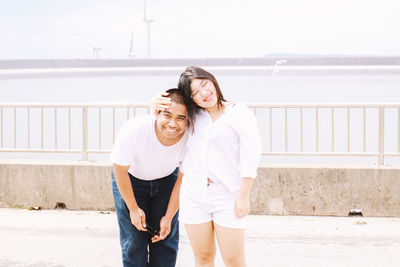 Young couple standing on footpath against railing and sea