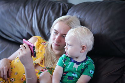 High angle view of mother showing phone to baby boy on bed at home