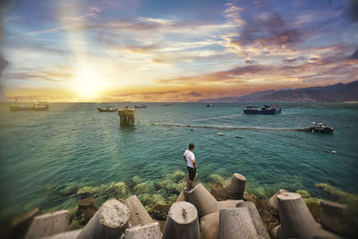 People standing on rocks by sea against sky during sunset