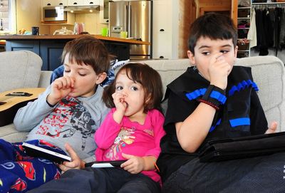Siblings sucking thumbs while sitting on sofa at home