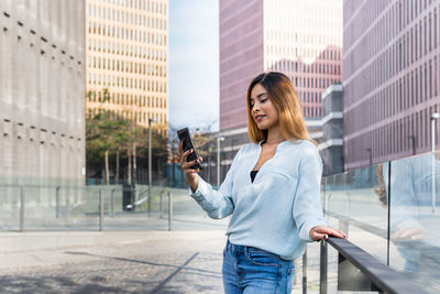 Smiling businesswoman using mobile phone standing against building