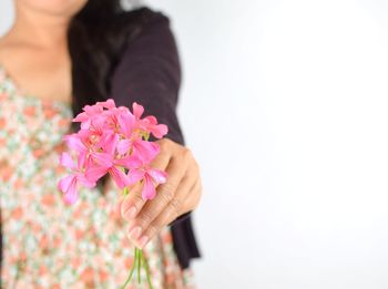 Midsection of woman holding pink flowers against white background