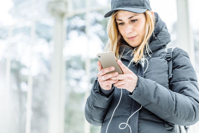 Young woman using mobile phone while standing in winter