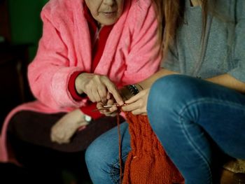 Midsection of mother assisting daughter in knitting wool at home