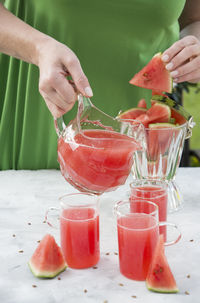 Young woman in a green dress pours a red refreshing drink from watermelon pulp into a glass 