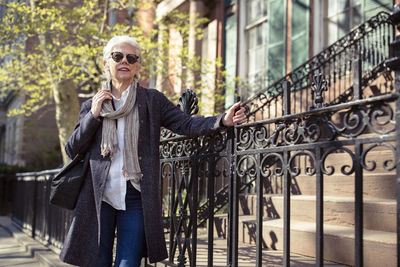 Thoughtful senior woman standing by metal railing on street