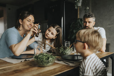 Happy mother showing smart phone to son while having food at dining table