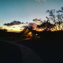 Silhouette buildings by road against sky during sunset