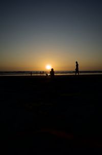 Silhouette people standing on beach against clear sky during sunset