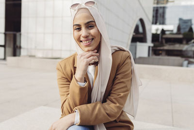 Smiling woman sitting with hand on chin at office park