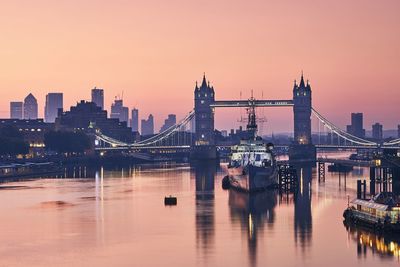 Bridge over river in city against sky during sunset