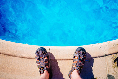Low section of man standing at poolside while wearing sandals