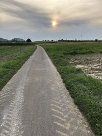 Empty road amidst field against sky