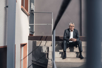 Senior businessman holding drinking glass on staircase