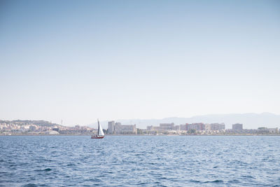 Sailboats in sea by buildings against clear sky