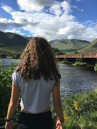 Rear view of girl standing by river against sky