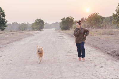 Smiling woman running with dog on road during sunrise