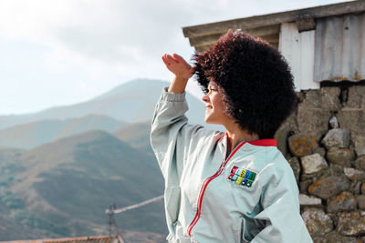 Afro woman shielding eyes while looking at view against mountains