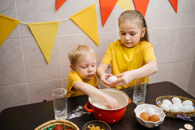 Girl breaks an egg into dough, brother helps cook, easter holiday