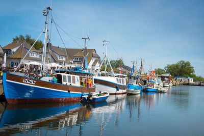 Boats moored at harbor against blue sky