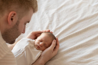 Close-up of man looking at newborn boy sleeping on bed at home