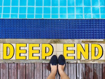 Low section of woman standing by yellow text on poolside