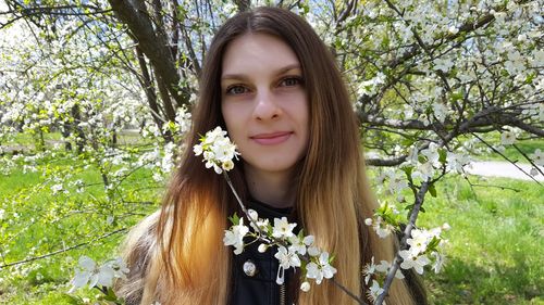 Portrait of smiling woman with long hair against cherry blossoms at park