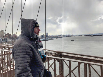 Side view of man standing on railing against sky