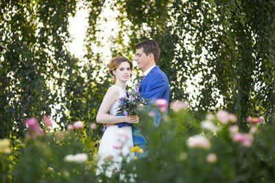 Side view of newlywed couple standing on grassy field at park