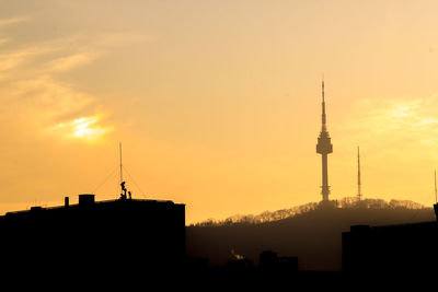 Silhouette of communications tower in city during sunset