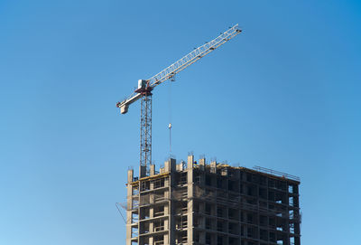 Low angle view of crane by building against clear blue sky