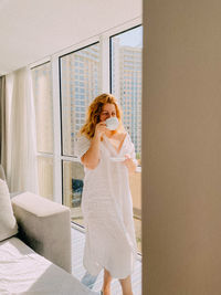 Rear view of young woman using mobile phone on bed at home