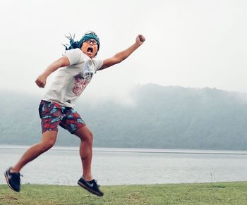 Young man with arms raised jumping on grassy lakeshore