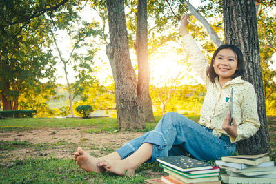 Portrait of smiling young woman sitting on tree trunk