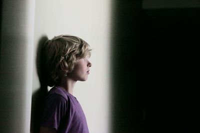 Side view of thoughtful girl standing against wall at home