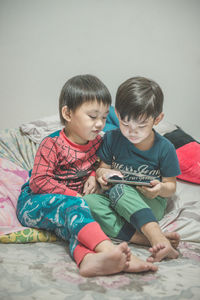 Cute siblings using phone while sitting on bed at home