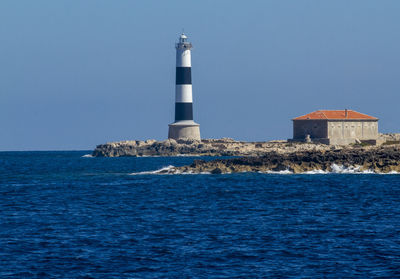 Lighthouse by sea against clear sky