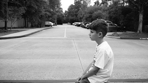 Side view of thoughtful boy sitting on road in city