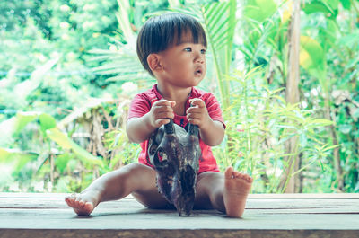 Full length of boy holding animal skull while sitting on wood