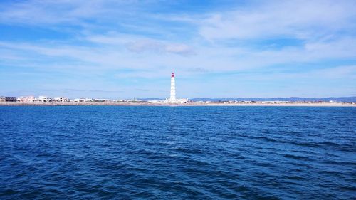 Lighthouse in sea against cloudy sky