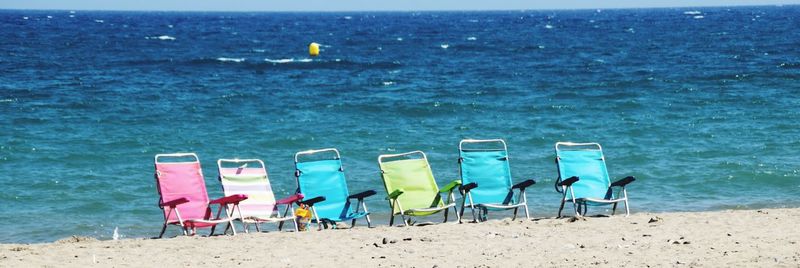 Deck chairs on beach against blue sky
