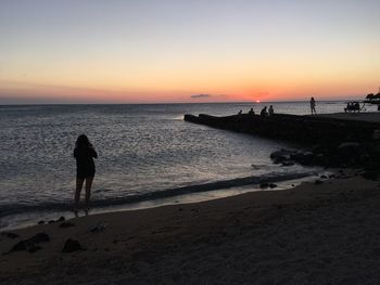 Silhouette woman walking on beach against sky during sunset