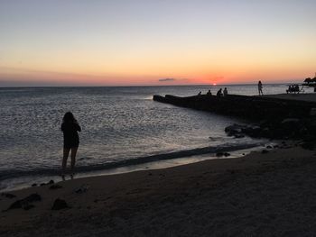 Silhouette woman standing on beach against sky during sunset