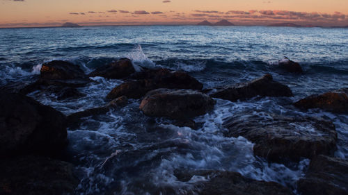 Rocks in sea against sky during sunset