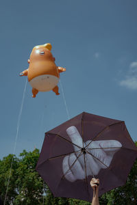 Cropped hand holding umbrella with middle finger by inflatable balloon