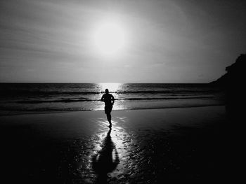 Silhouette man running at beach against sky during sunset